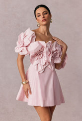 Woman wearing a pink dress with floral embellishments against a plain background