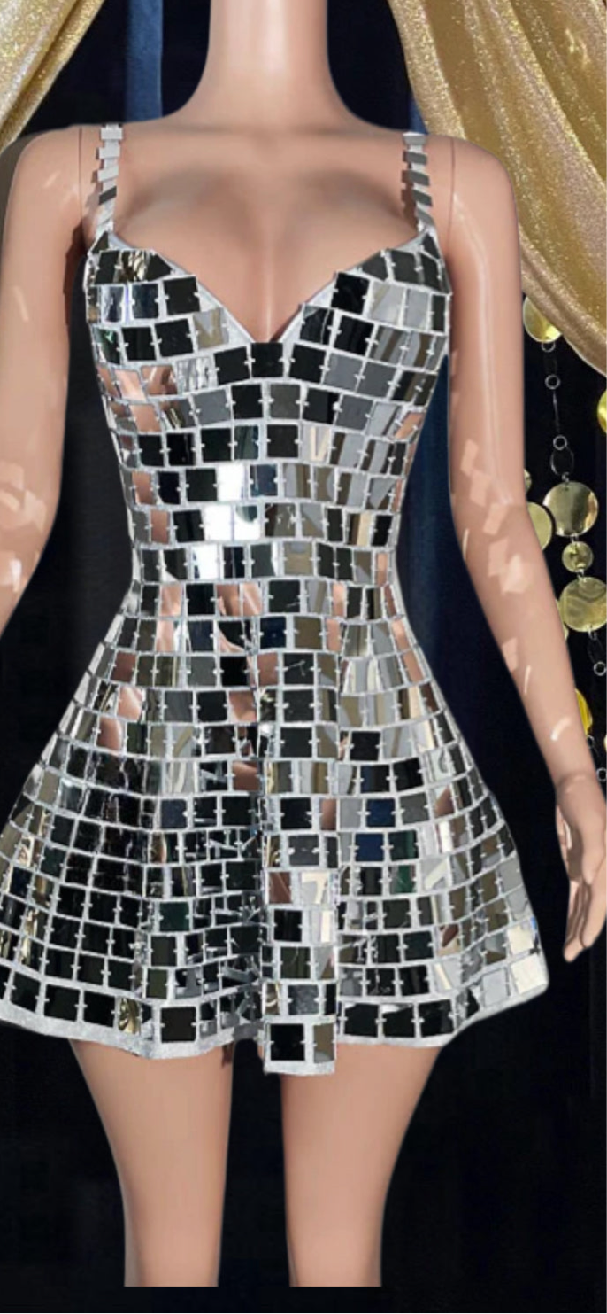Woman wearing a shimmering mirror dress reflecting light, standing in a festival-like setting.