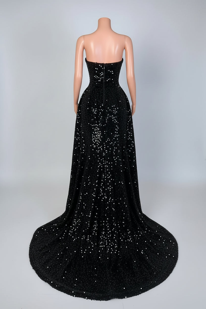 Black strapless evening gown with a long train on a mannequin against a decorative wall.
