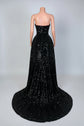 Black strapless evening gown with a long train on a mannequin against a decorative wall.