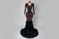Black lace evening gown with feathered skirt on a white marble floor.