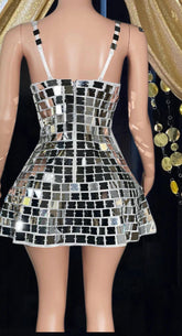 Woman wearing a shimmering mirror dress reflecting light, standing in a festival-like setting.